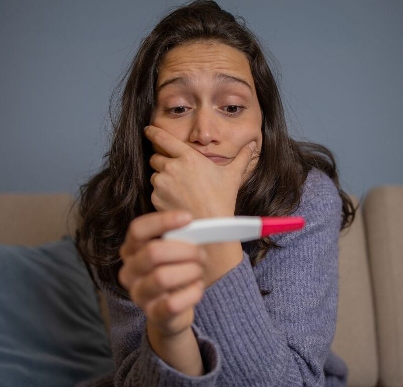 A woman holding a pregnancy test wondering how soon she can take a test.